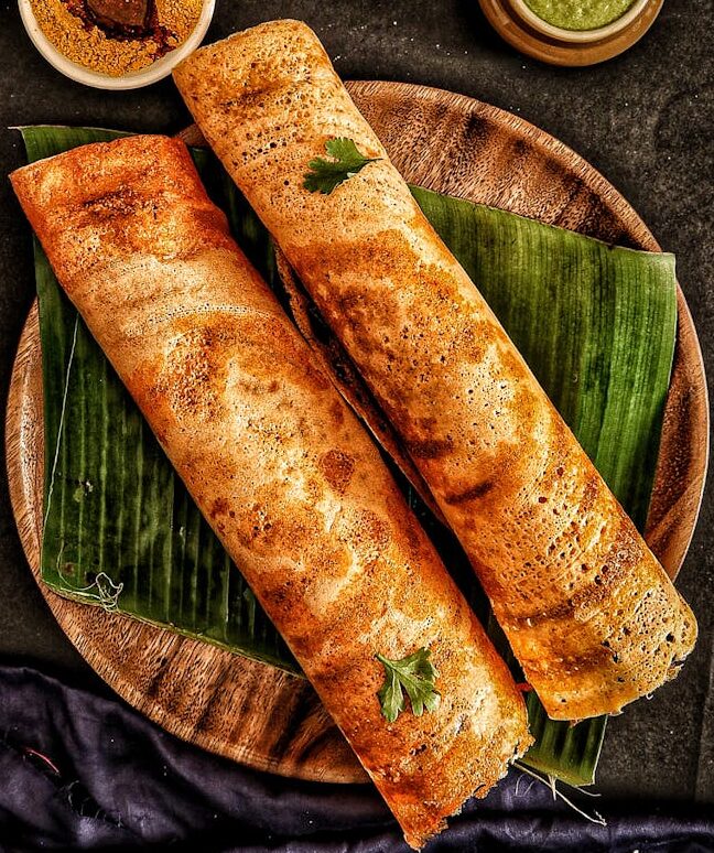 Delicious traditional dosa served with a variety of Indian chutneys and sambar on banana leaves.