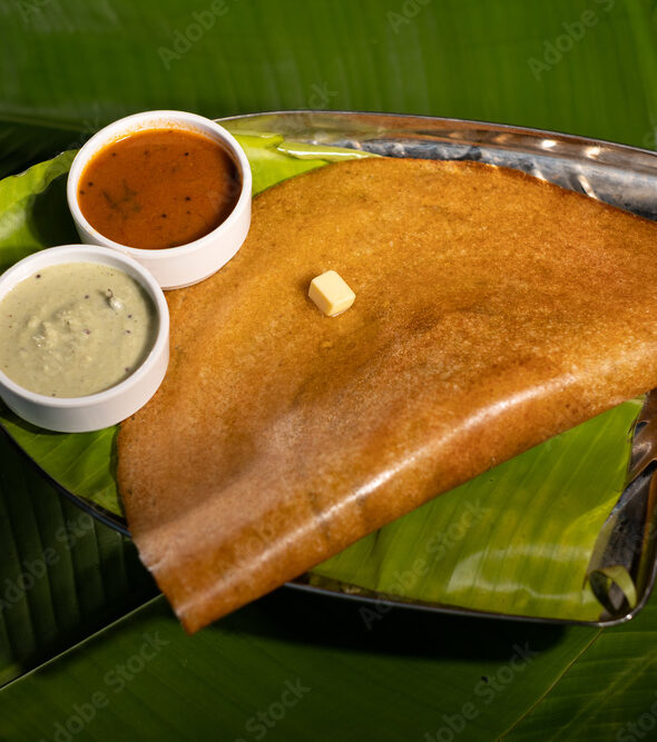 A masala dosa served with sauces and topped with a cube of butter.